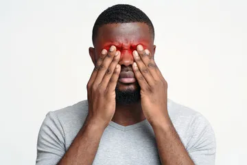 A man holding his hands over his eyes, which are red and inflamed, depicting the discomfort of a bacterial or viral eye infection.